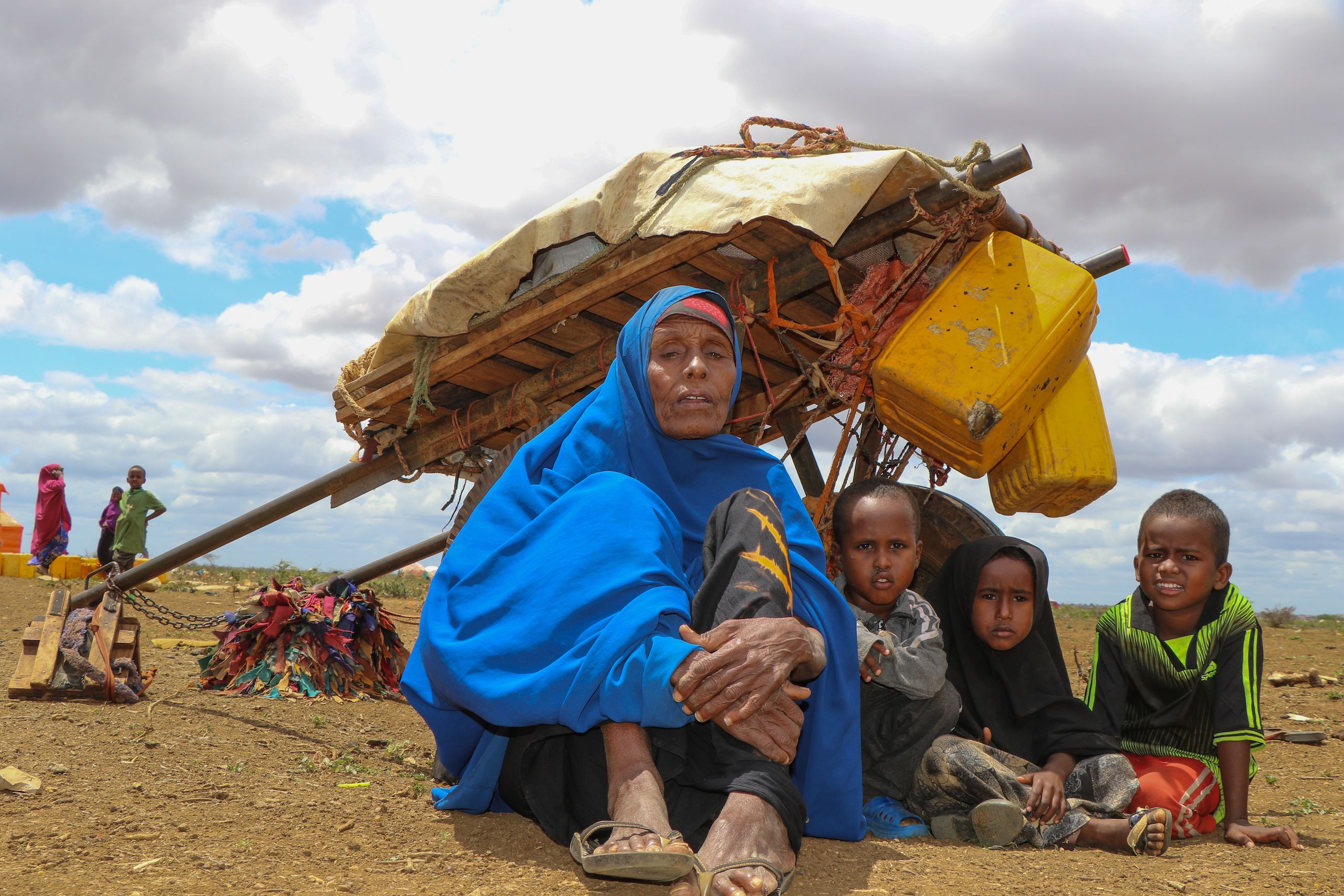 A grandmother sits with three young children next to a donkey cart ina desert region.