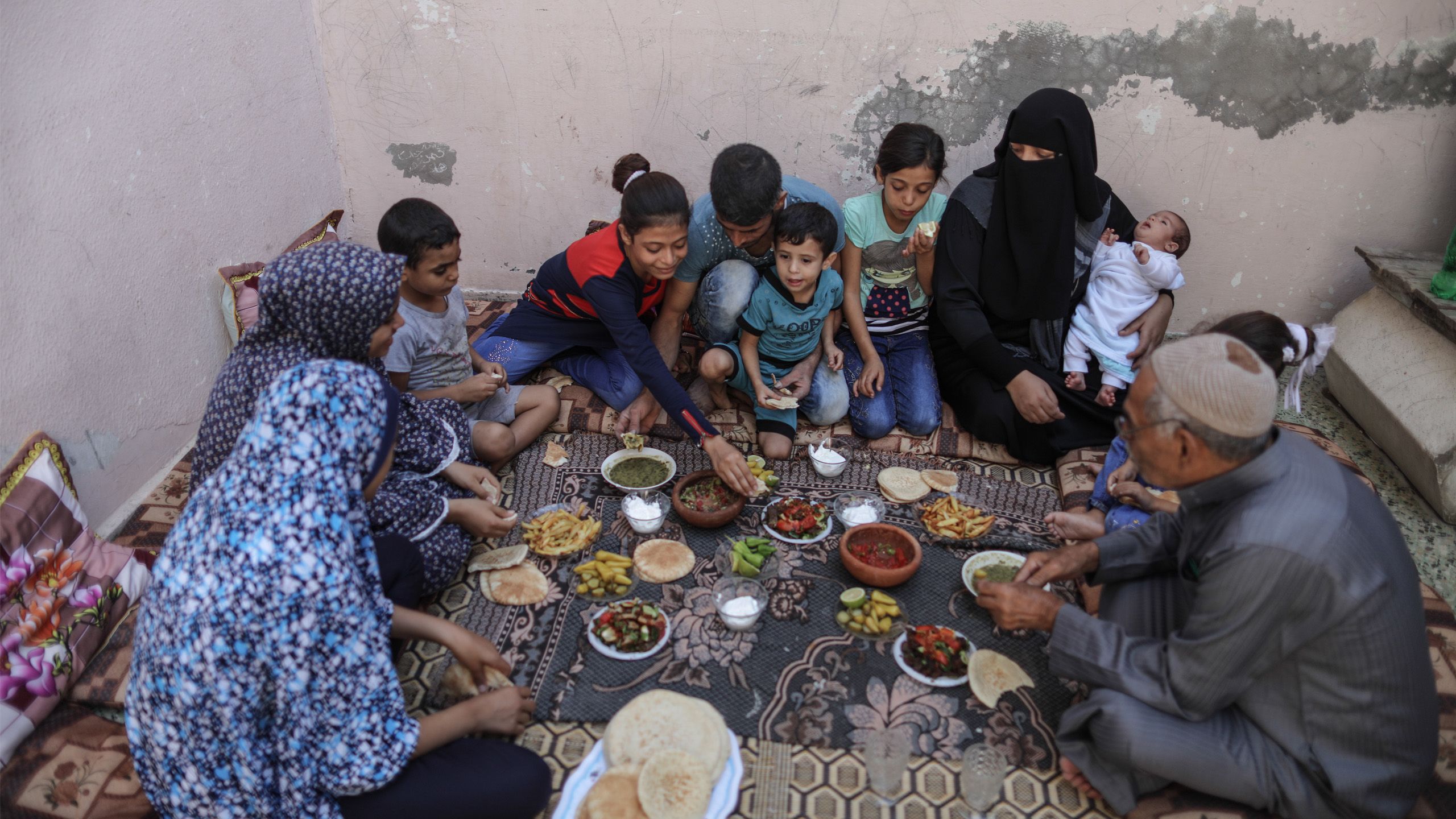 A Palestinian family having lunch together. The food is placed on a rug on the floor.