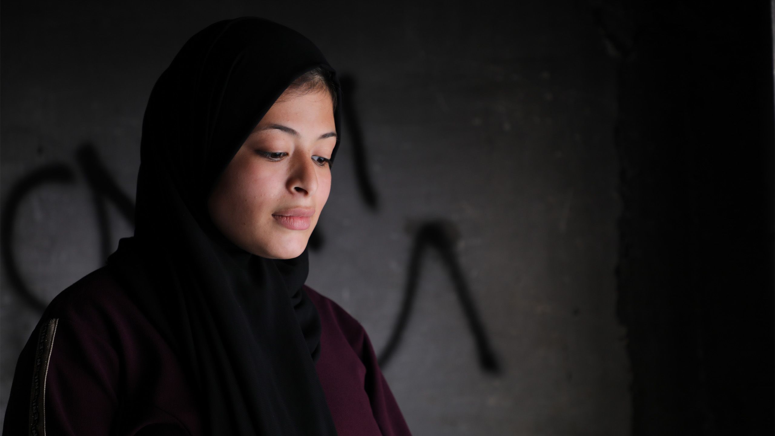 Portrait of Omaia, a 16-year-old Palestinian girl. She is wearing all black, and she is gazing at something in front of her.