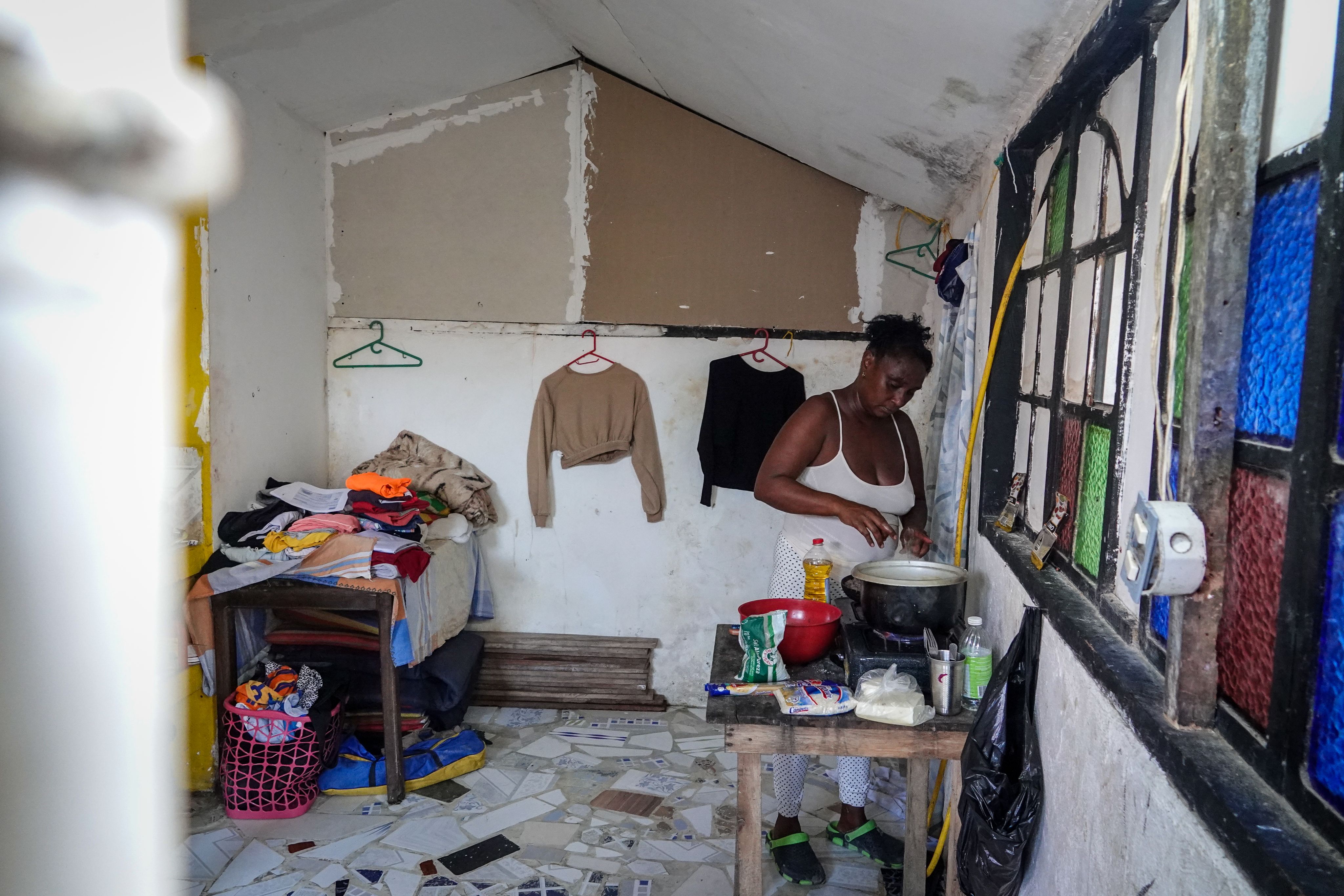 Petra standing by a pot and adding ingredients. She is surrounded by clothing hanging on the walls on lying on a nearby table.