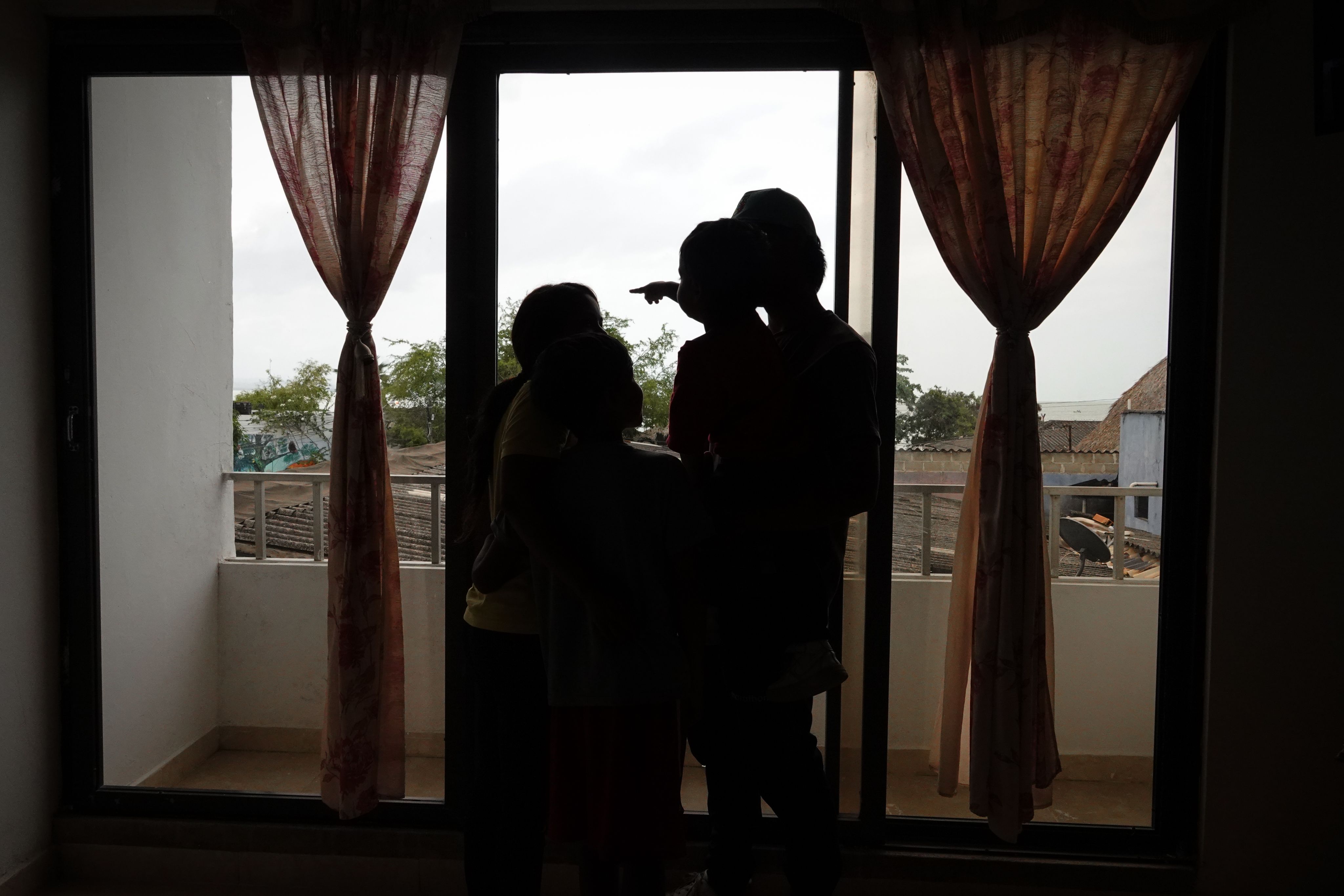 Silhouette of a man, woman, and two children standing by a window.