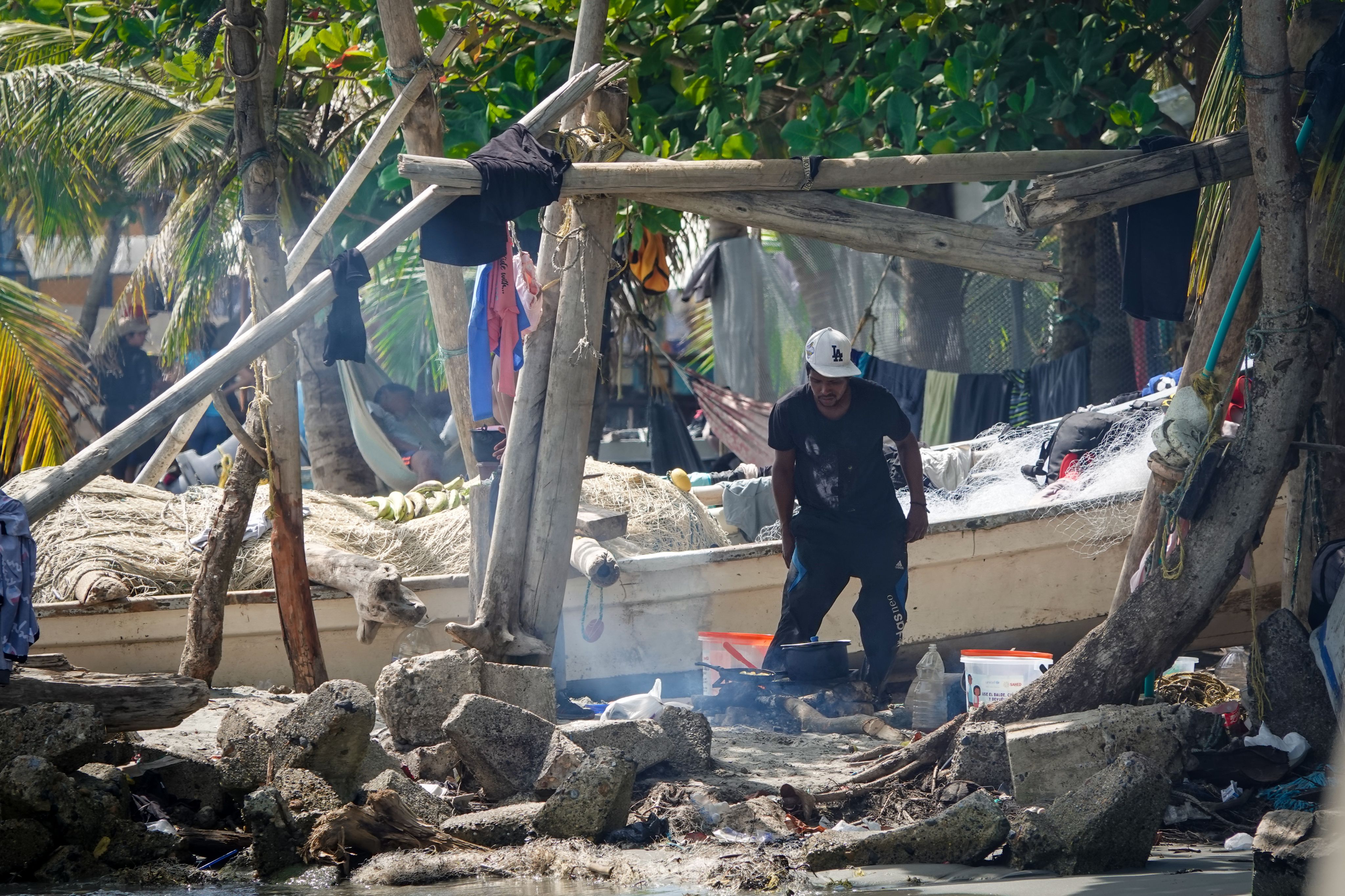 A man cooking on the beach surrounded by his belongings. 